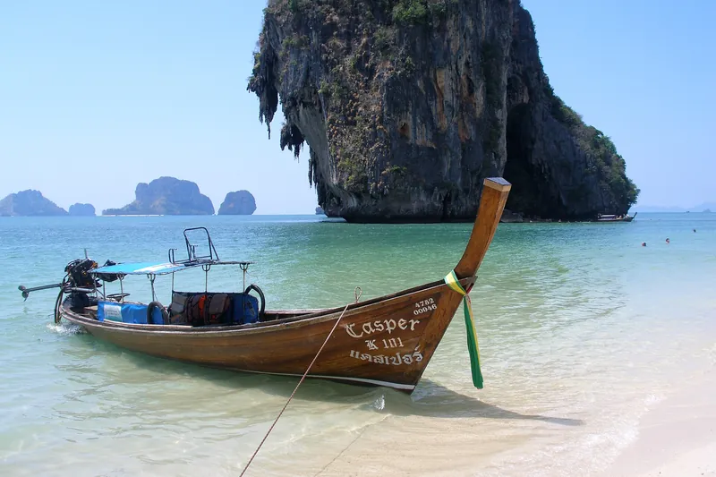 Longtail boat on turquoise water below Railay's limestone cliffs