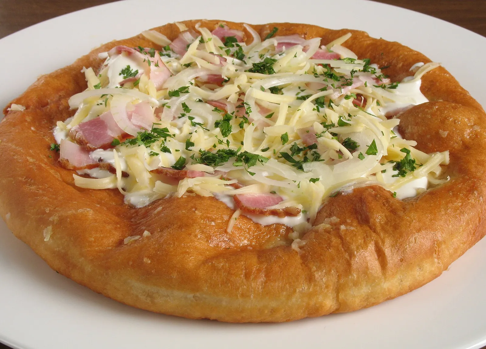 Golden lángos topped with cheese, ham and herbs
