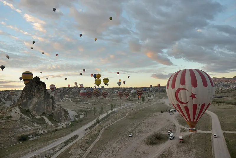 Dozens of hot-air balloons rising over Cappadocia at dawn