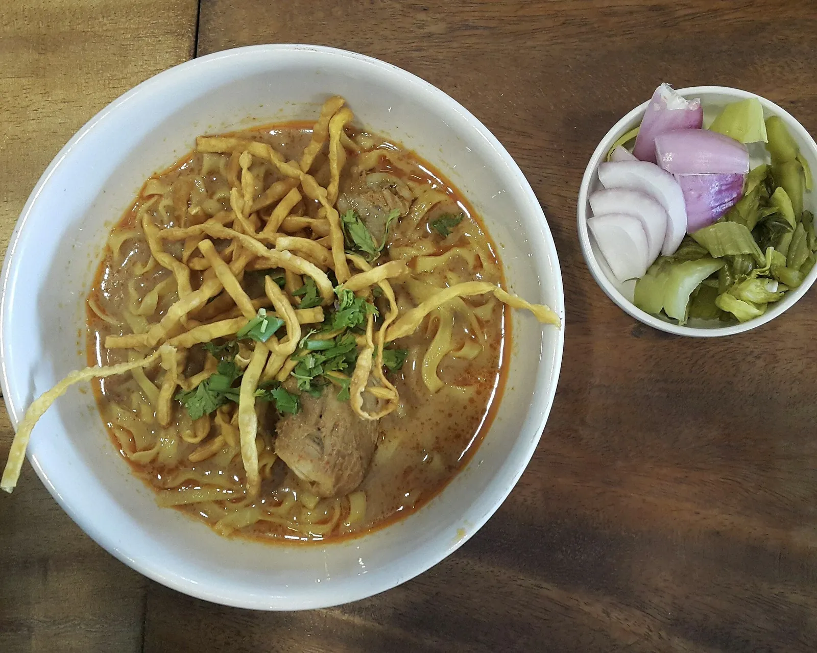 A bowl of khao soi with pickles and shallots