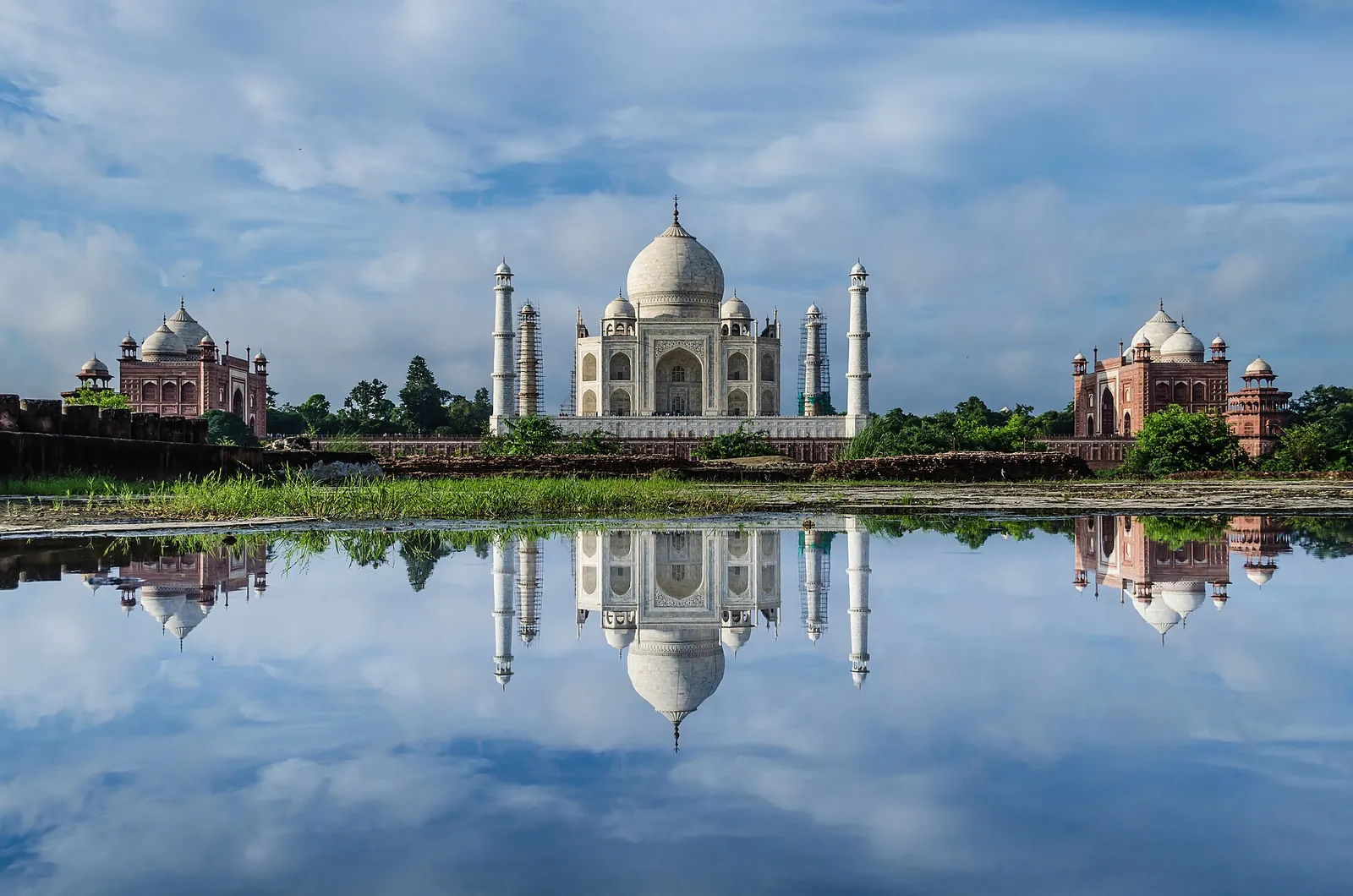 The Taj Mahal reflected in still water under a cloudy blue sky