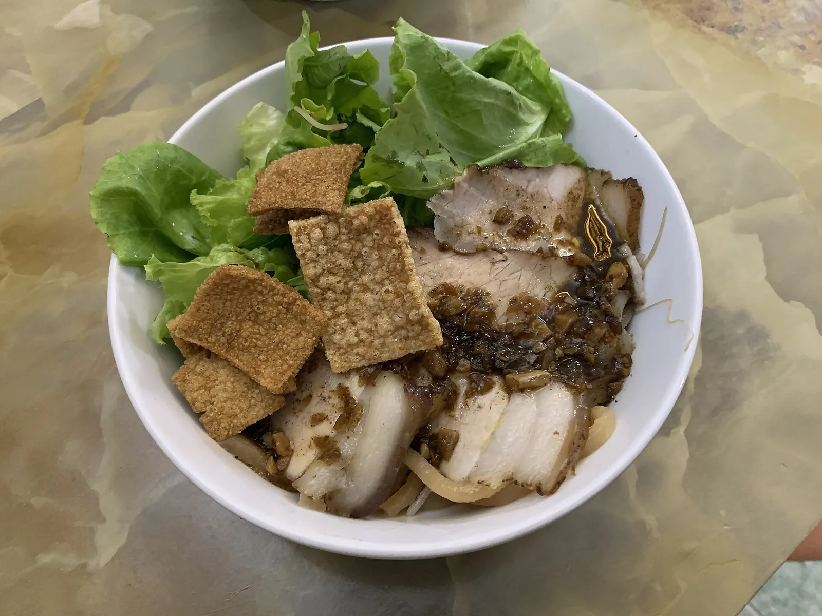 A bowl of cao lau noodles with pork and greens