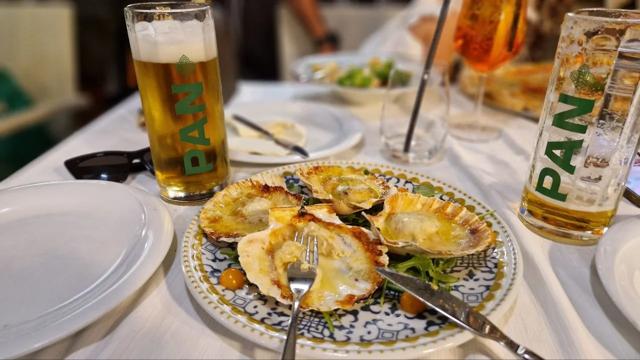Dinner in Rovinj: a plate of baked scallops with two glasses of Croatian Pan beer on a white tablecloth