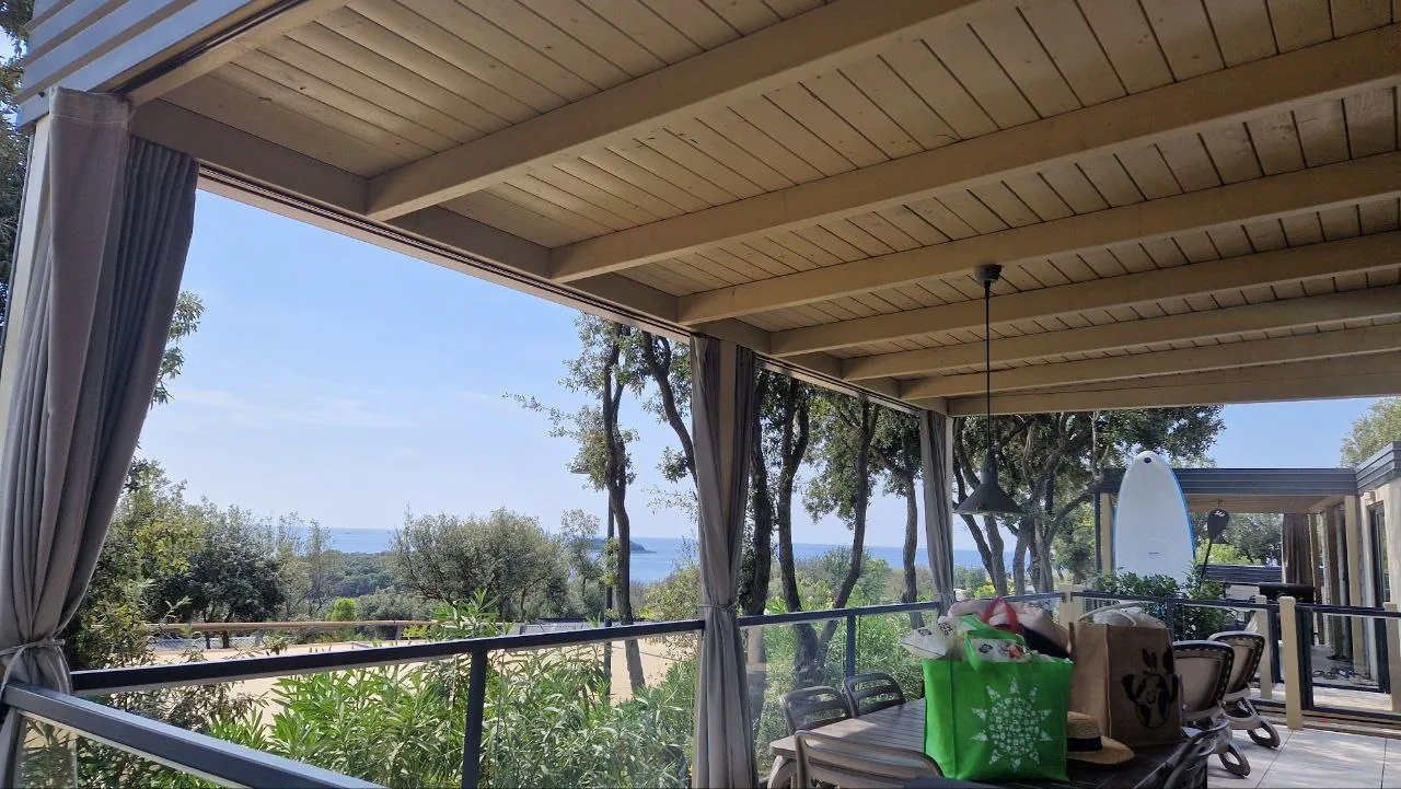 The covered wooden terrace of our camping home, looking out over pine trees towards the sea