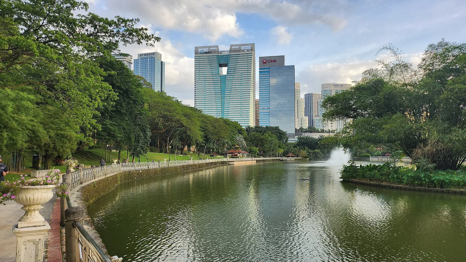 Leafy lake in Perdana Botanical Garden with city towers beyond