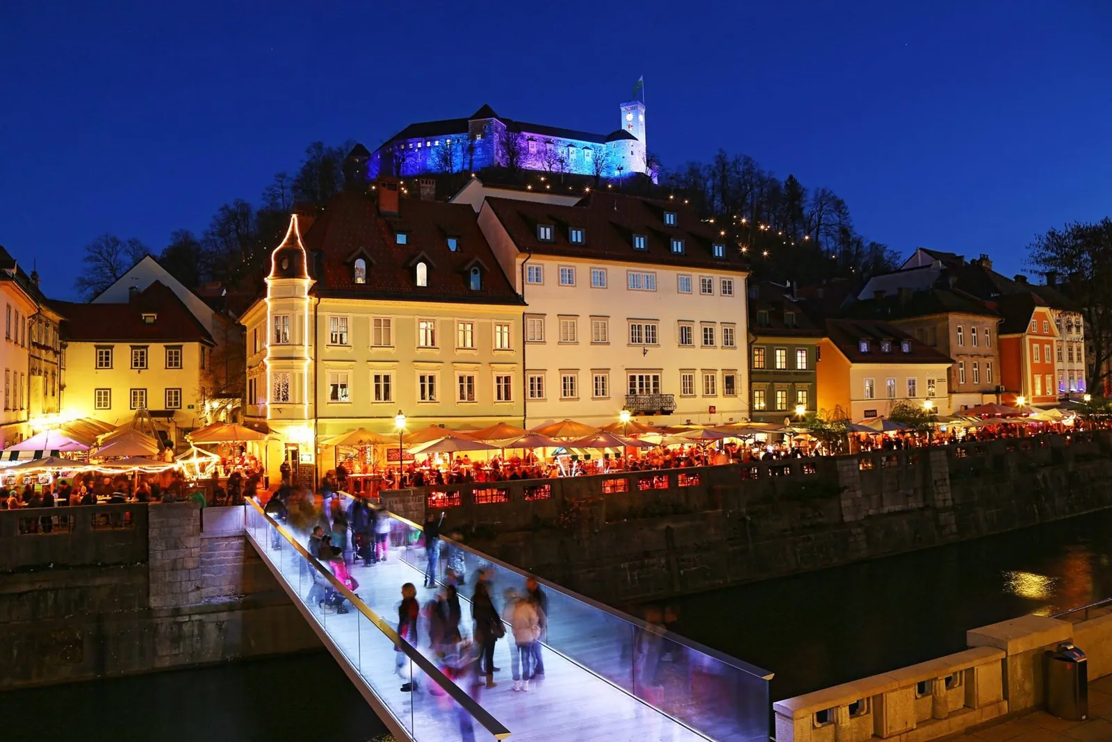 The Ljubljanica riverbank glowing at night below the castle