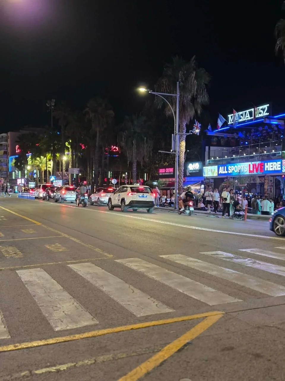 Lloret de Mar's nightlife strip after dark, with palm trees, neon signs and sports bars