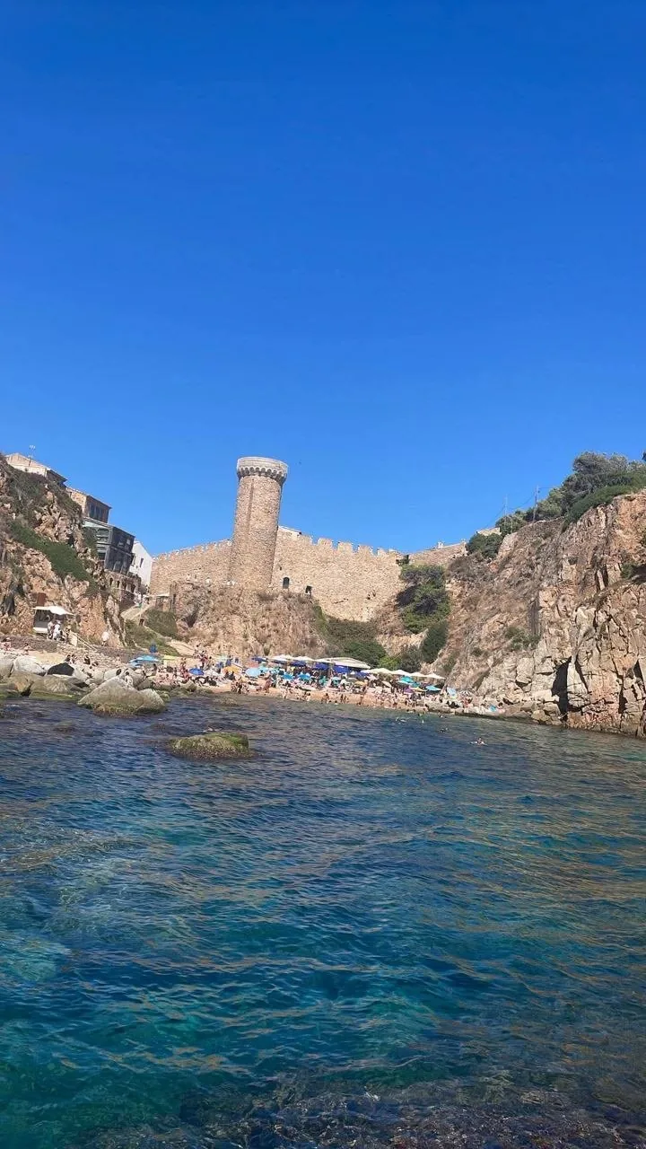 The round medieval tower of Tossa de Mar's walls above the rocks and clear turquoise water