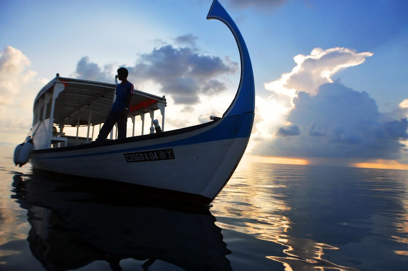 A dhoni boat on glassy water at sunset