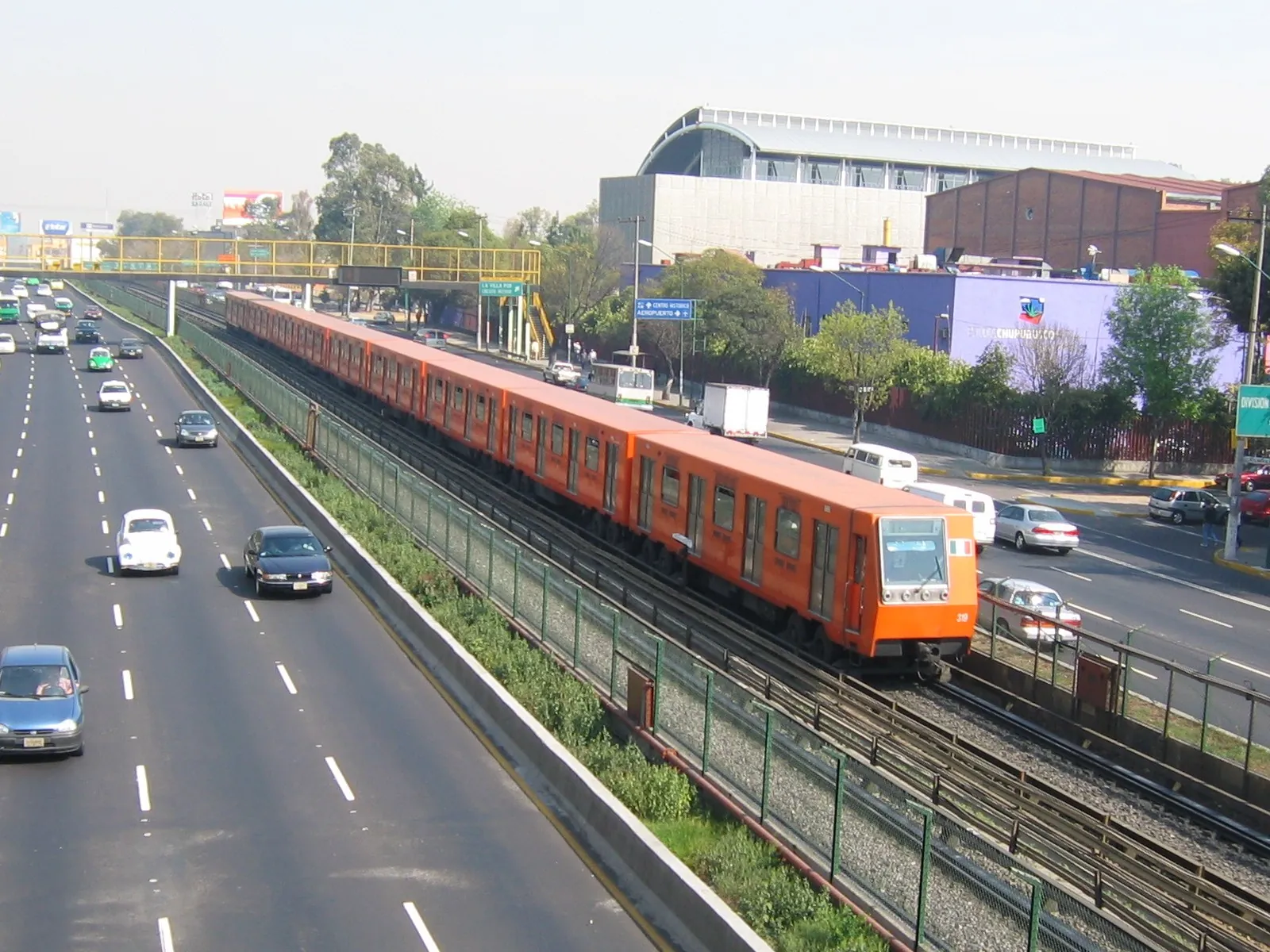 An orange Mexico City Metro train beside a busy road