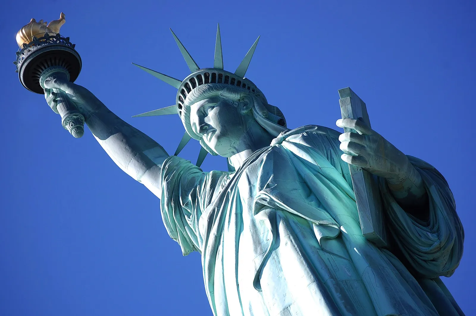 Statue of Liberty raising her torch against a blue sky