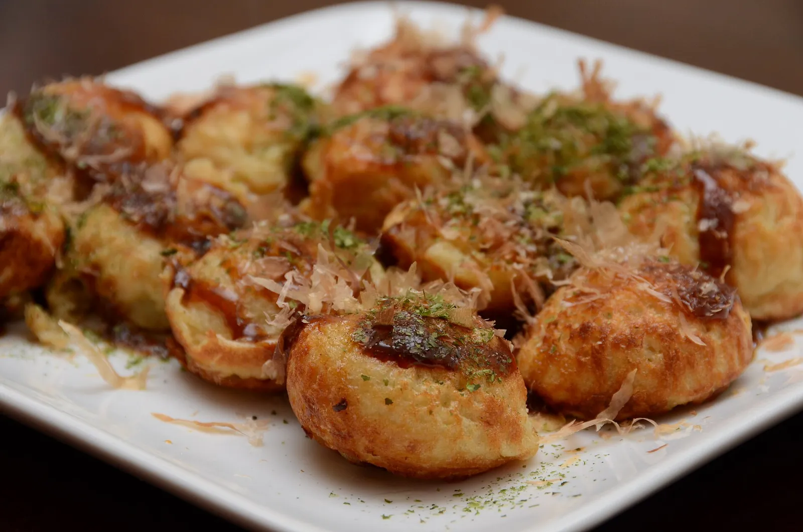 A plate of takoyaki topped with sauce and bonito flakes