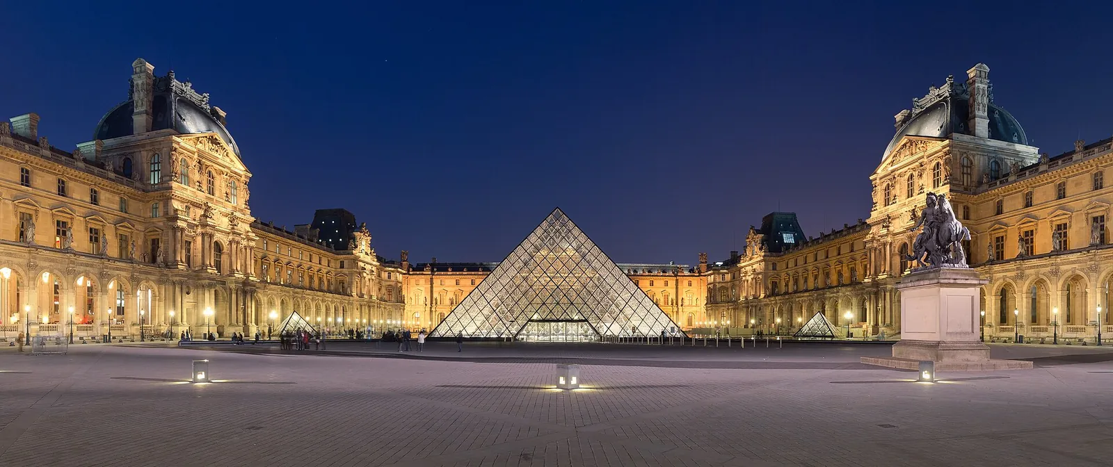 Louvre pyramid glowing at dusk in the Cour Napoléon