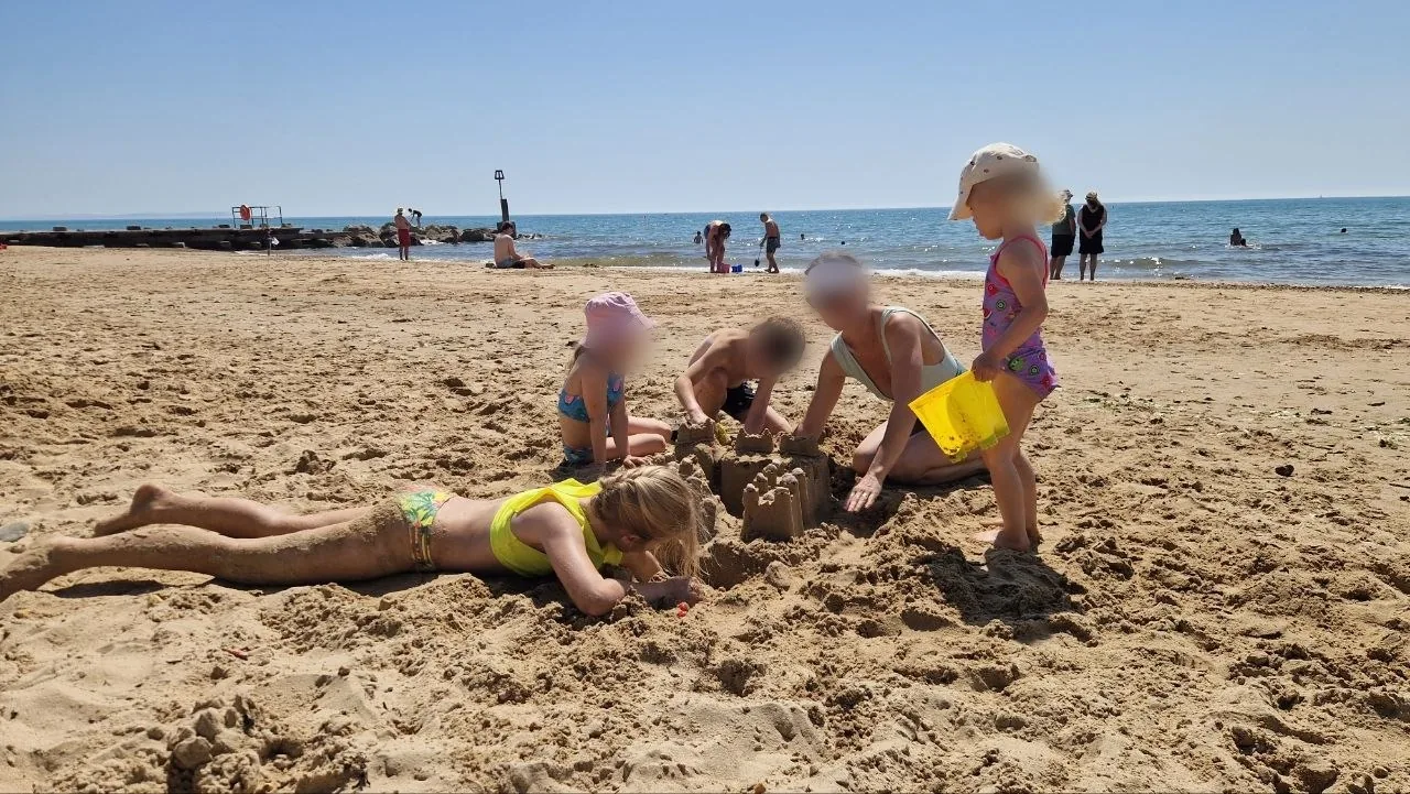 Children building a sandcastle with buckets on the wide sandy beach at Bournemouth on a hot July day