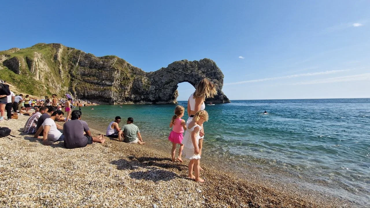 Durdle Door's natural limestone arch over turquoise water, with families on the pebble beach in front