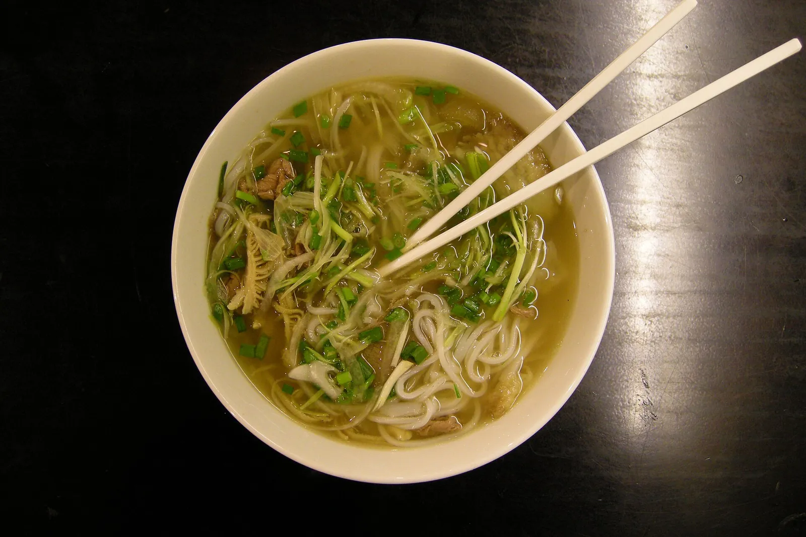 A steaming bowl of pho with chopsticks