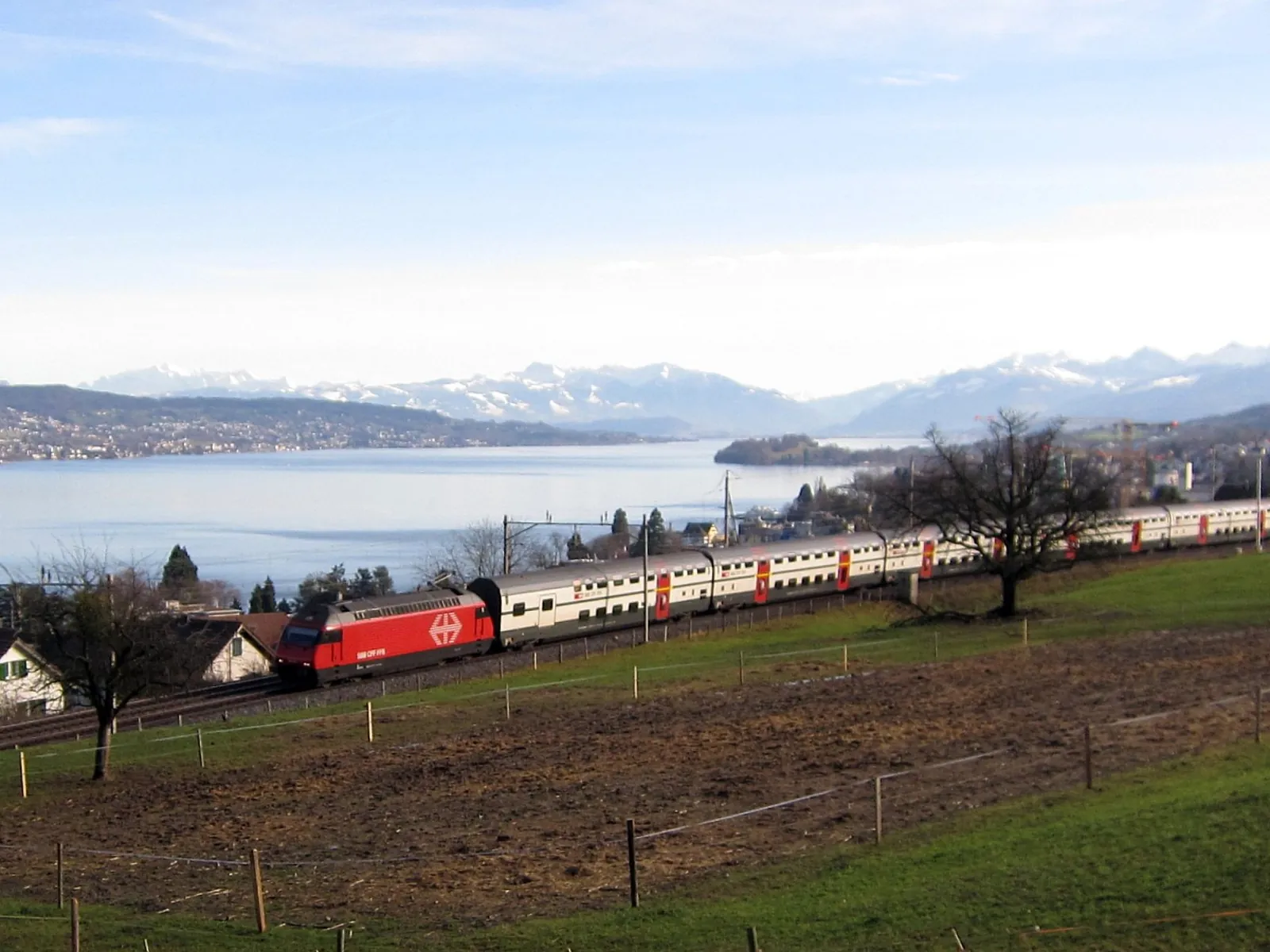 A red Swiss train running along Lake Zurich below the Alps